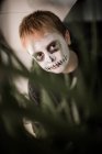 Junge mit Totenkopf-Gesicht versteckt sich hinter Pflanzen — Stockfoto