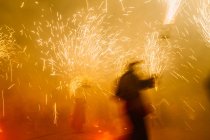 Bright sparkling fireworks and blurred silhouette on night street celebration scene — Stock Photo