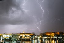 Night cityscape with stormy lightning in dark sky after rain. — Stock Photo