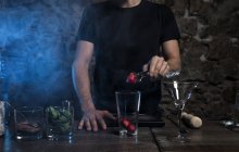 Mains masculines mettant la fraise dans un verre à cocktail — Photo de stock