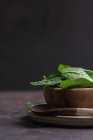 Immagine ritagliata di piatto di legno pieno di foglie di spinaci freschi e cucchiaio rustico sul tavolo — Foto stock
