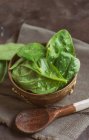 Top view of wooden bowl  filled with fresh spinach leaves with spoon on rural towel — Stock Photo