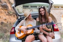 Girls sitting with guitar in car trunk — Stock Photo
