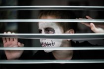 Boy with skull face painting looking through sunblind — Stock Photo