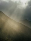 Picturesque view of sun rays penetrating clouds in gloomy sky above mountains range. — Stock Photo