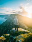 Rückansicht eines Mannes, der auf bemoosten Felsen über Bergen und Meer in gleißendem Sonnenlicht steht. — Stockfoto