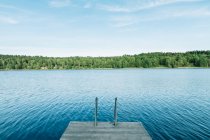 Wooden pier and blue lake water with forest on shore. — Stock Photo