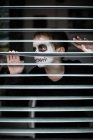 Boy with skull face painting looking through sunblind — Stock Photo