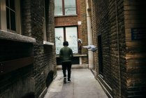 Habitante anónimo caminando por callejón pavimentado entre edificios antiguos . - foto de stock