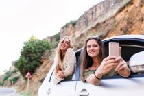 Amigos olhando pelas janelas do carro e tirando selfie — Fotografia de Stock