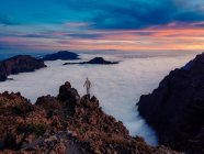 Voyageur debout sur le rocher avec un fond de ciel couchant coloré et des montagnes dans le brouillard . — Photo de stock