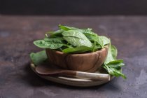 Close up view of wooden bowl filled with fresh spinach leaves and rustic spoon on table — Stock Photo
