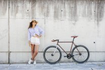 Menina de chapéu posando perto de bicicleta — Fotografia de Stock