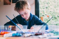 Блондинка молодий хлопчик малює акрилами — стокове фото
