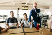 Cheerful waiter man serving drinks to friends at table in bar. — Stock Photo