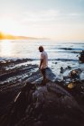 Seitenansicht von Mann mit Sonnenbrille posiert mit Kamera auf Küstenfelsen — Stockfoto