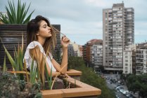 Чуттєва жінка позує на балконі з фасадами будівель на фоні — стокове фото