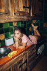 Чуттєва жінка лежить на кухонній стійці з посудом і бананами і дивиться на камеру — стокове фото