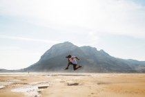 Вид збоку на людину, що позує у стрибку на піщаному пляжі — стокове фото