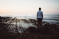 Rückansicht eines Mannes, der an der Küste auf einem Felsen posiert — Stockfoto