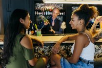 Женщины сидят за барной стойкой, пока бармен готовит напитки — стоковое фото