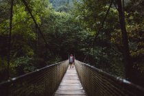 Homme avec planche à roulettes posant sur un pont de corde en forêt — Photo de stock
