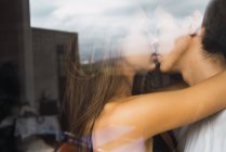Jovem casal beijando atrás da janela em casa — Fotografia de Stock