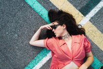 From above view of brunette woman in sunglasses lying on lines of asphalt road. — Stock Photo