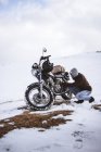 Man adjusting motorcycle's engine in snowy highlands — Stock Photo