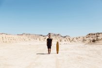 Человек в черной одежде стоит возле скейтборда в пустыне — стоковое фото