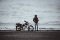 Man in helmet posing by motorcycle in snowy road — Stock Photo