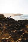 Mann sitzt auf Klippe über Küstenlandschaft — Stockfoto