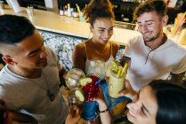 Веселые друзья, звенящие коктейлями в баре — стоковое фото