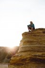 Tourist man sitting on cliff in back lit and looking away — Stock Photo