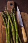 Top view of green asparagus with rural knife on wooden board — Stock Photo