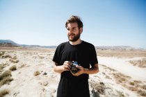 Portrait d'homme barbu posant avec caméra sur désert — Photo de stock