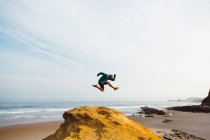 Vue latérale de l'homme posant en saut sur une falaise sur fond de scène côtière — Photo de stock