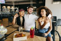 Мужчина и две веселые девушки делают селфи за столиком в кафе — стоковое фото