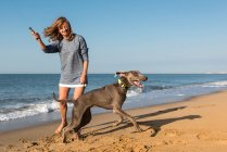 Взрослая женщина играет с собакой на пляже — стоковое фото