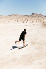 Visão traseira do homem andando de skate no deserto no dia ensolarado — Fotografia de Stock