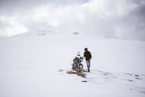 Man walking by motorcycle in snowy highlands — Stock Photo