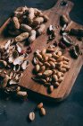 Close up view of pile of peanuts and peels on wooden cutting board on dark surface — Stock Photo