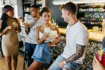 Cheerful friends drinking cocktails by bar counter — Stock Photo