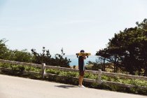 Вид збоку людини, що тримає скейтборд на плечі і захоплюючий морський пейзаж — стокове фото