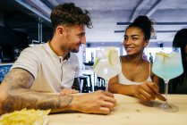 Smiling couplesitting in bar with cocktails and looking at each other — Stock Photo