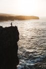 Vista à distância da silhueta da pessoa de pé no penhasco sobre o mar — Fotografia de Stock
