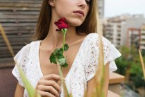 Чувственная женщина, позирующая с красной розой на балконе — стоковое фото