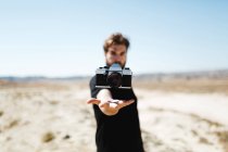Analog camera flying over outstretched hand of man standing in desert on sunny day. — Stock Photo