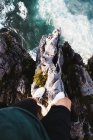 Дивлячись вниз погляд людини, що стоїть на краю скелі над жорсткими сонячними світлими океанськими хвилями — стокове фото