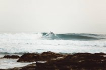 Vista lateral del surfista atrapando olas en la orilla del mar - foto de stock
